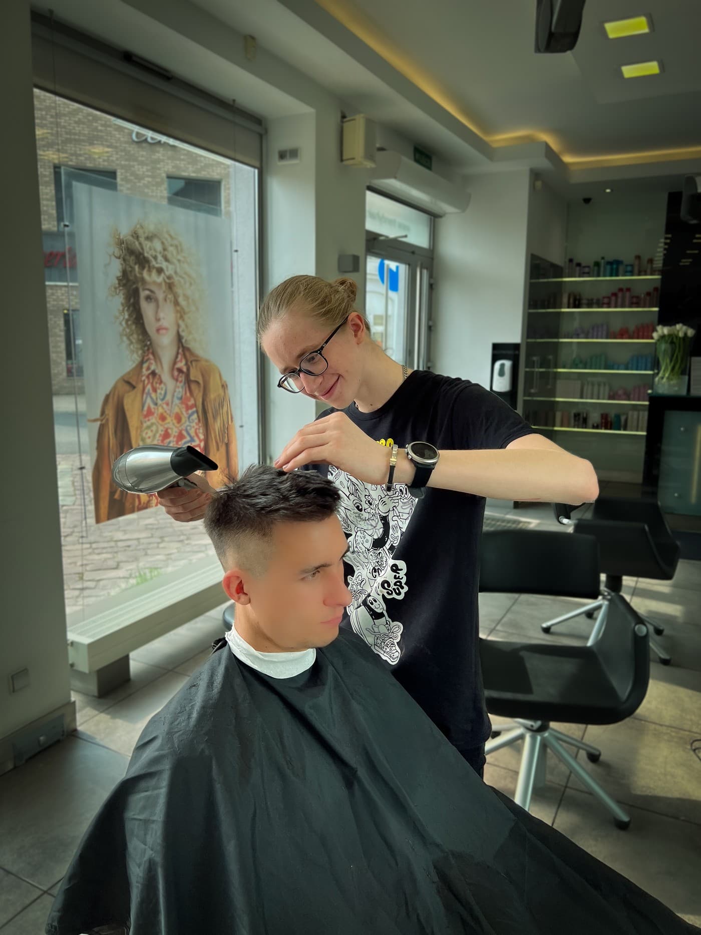Damian suszący włosy klienta suszarką w jasnym salonie fryzjerskim
